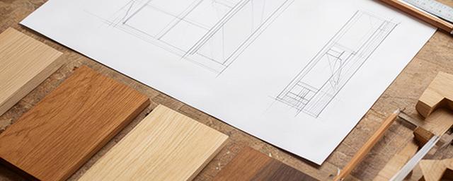 Disegno tecnico di un mobile in legno accanto a campioni di essenze sul tavolo da lavoro